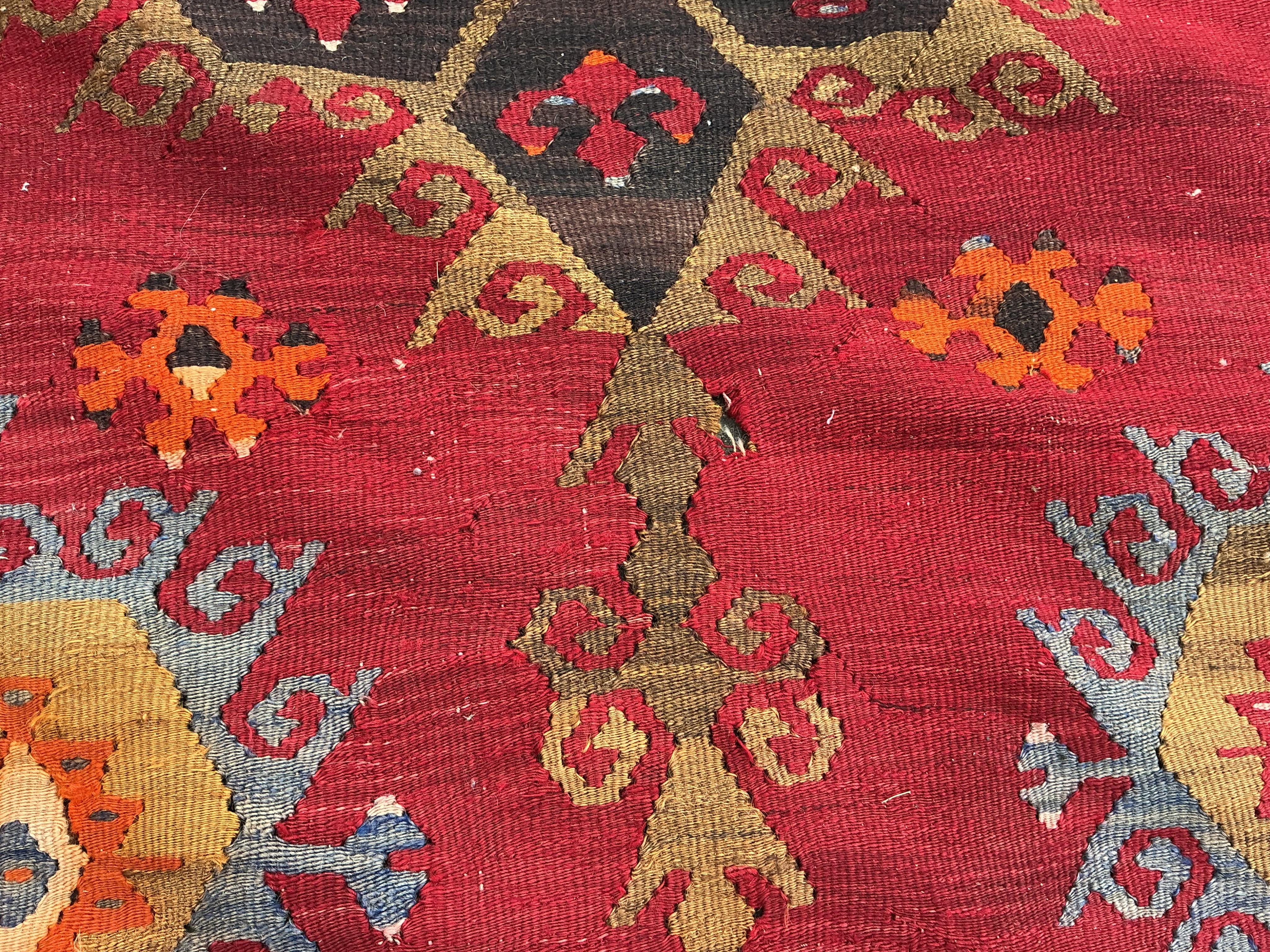 A Turkish Anatolian polychrome flatweave Kilim carpet, woven with geometric lozenges on a red field, 367 x 292cm